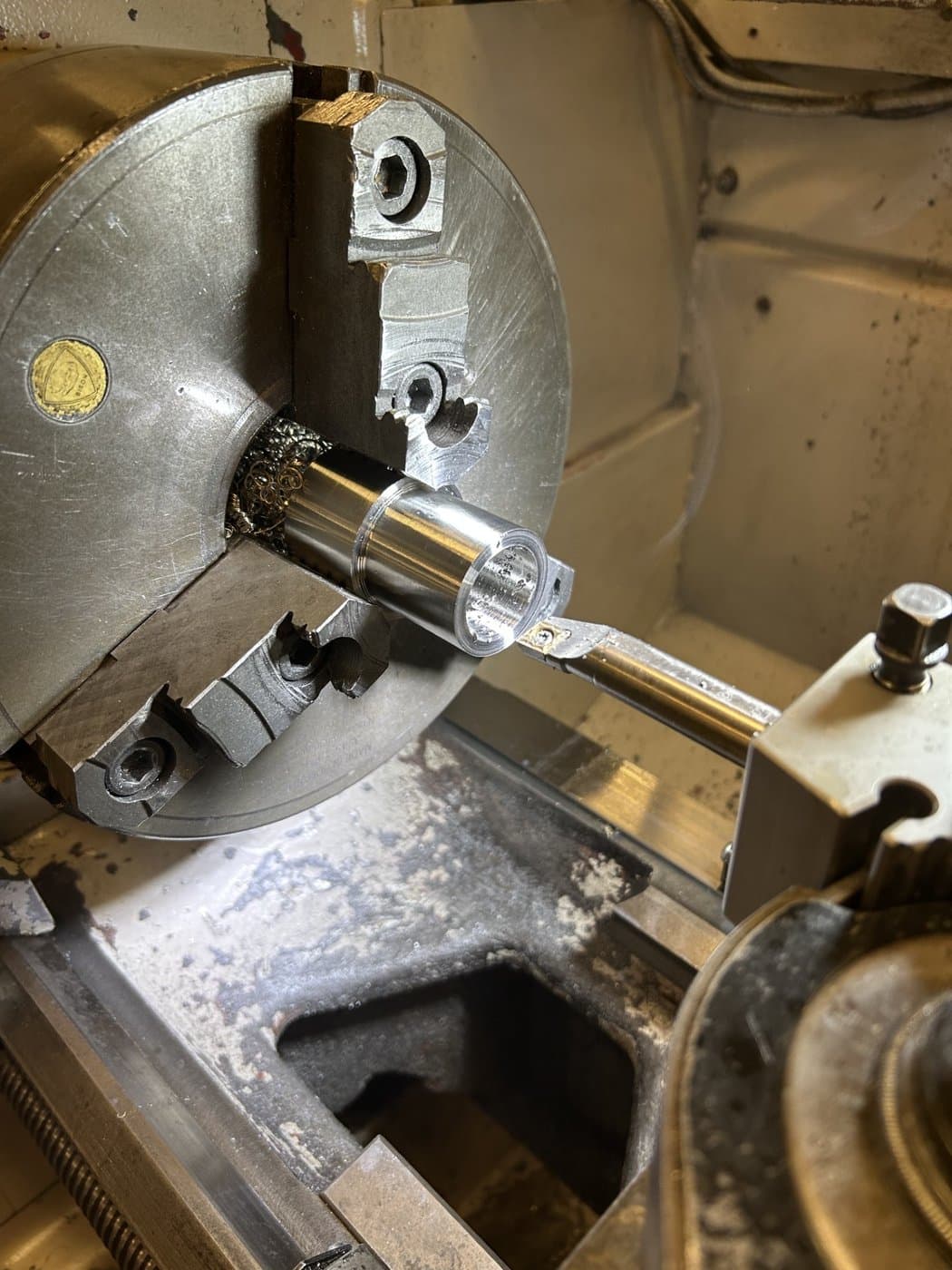 Aluminum stock spinning in a three-jaw lathe chuck, turning tool engaged