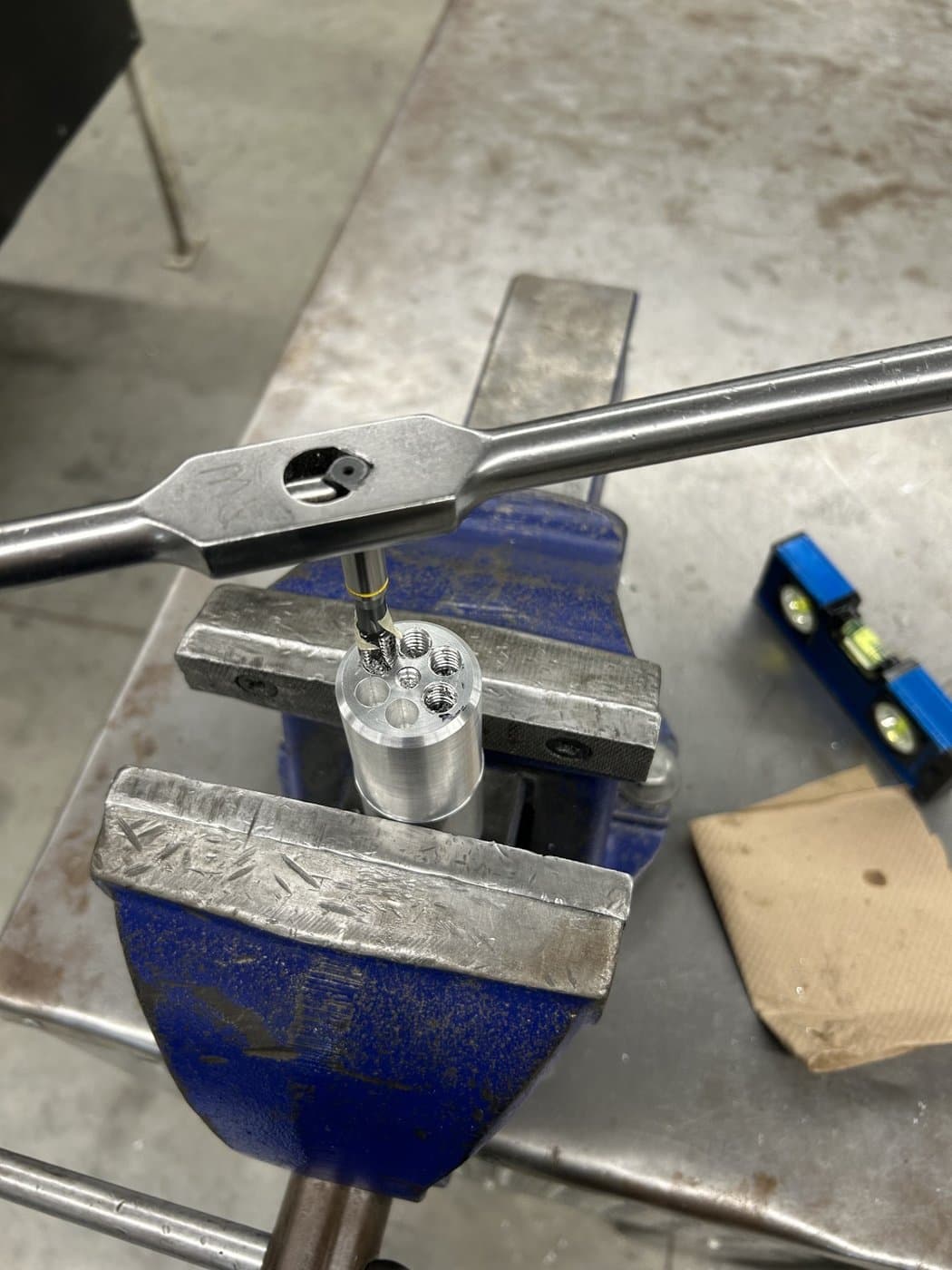 Hand-tapping threads into a machined aluminum part held in a bench vise